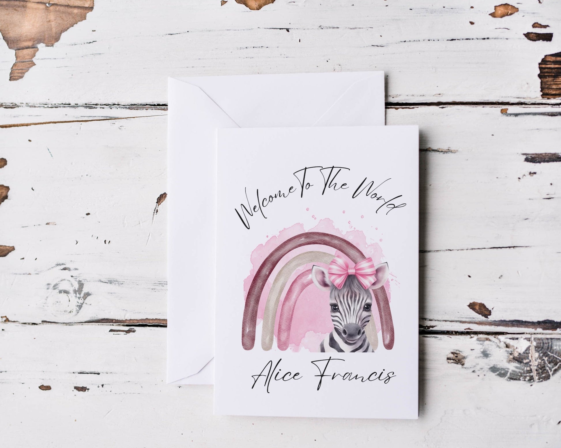 A white card with a graphc of a Zebra standing in front of a rainbow with the words Welcome To The World personalised with a baby's name.