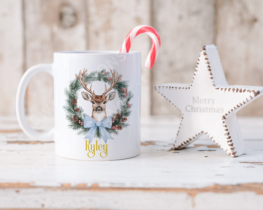 A festive Christmas mug featuring a reindeer design surrounded by a decorative wreath.