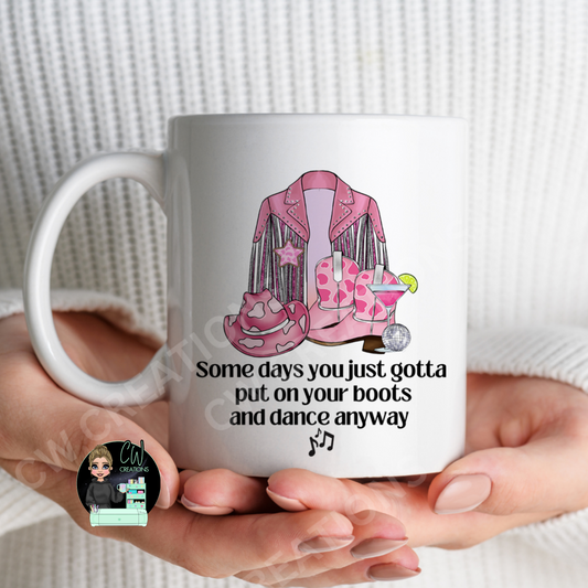  A cowgirl mug featuring a quote saying some days you just gotta put your boots on and dance anyway.
