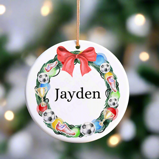 A ceramic Christmas decoration with a football wreath with a red ribbon personalised with a name.