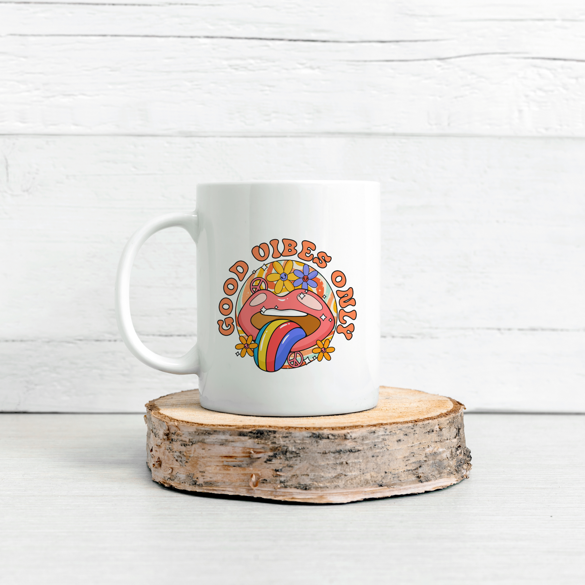 A white mug with a bright mouth graphic with tongue sticking out and with flowers around design reading the words Good Vibes Only.