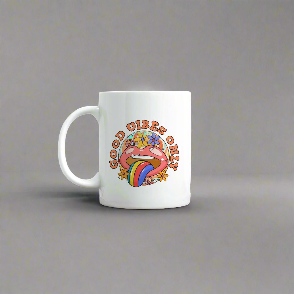 A white mug with a bright mouth graphic with tongue sticking out and with flowers around design reading the words Good Vibes Only.