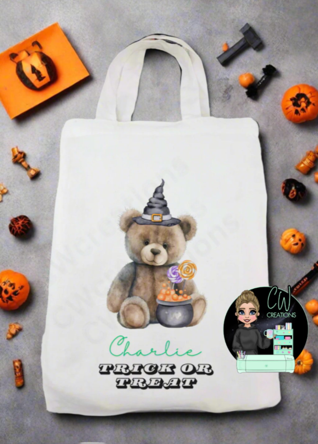 A white bag with a teddy wearing a witches hat sitting in front of a cauldron.