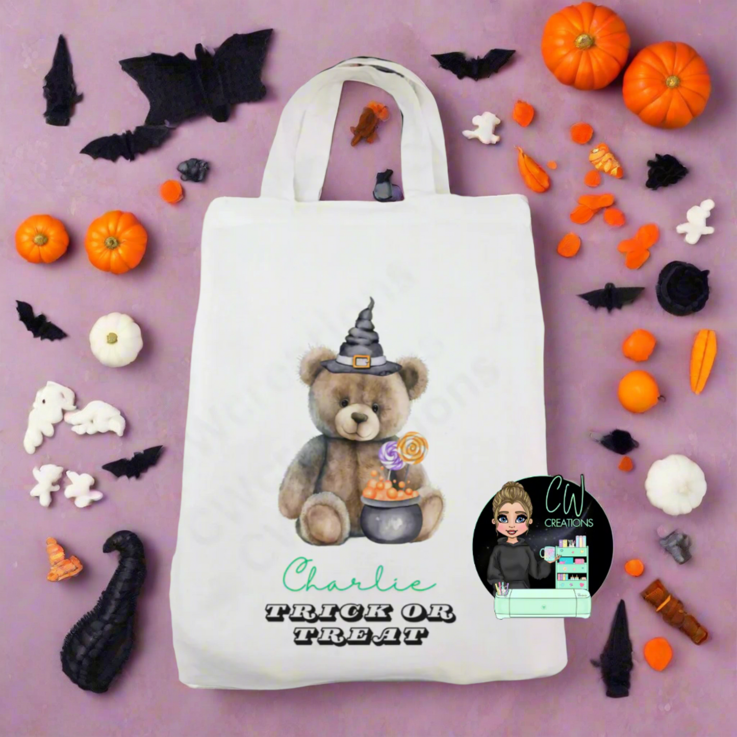 A white bag with a teddy wearing a witches hat sitting in front of a cauldron.