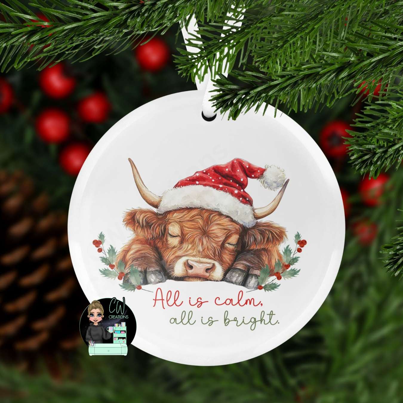 A round christmas decoration with a graphic of a sleeping highland cow with the words All is calm all is bright.