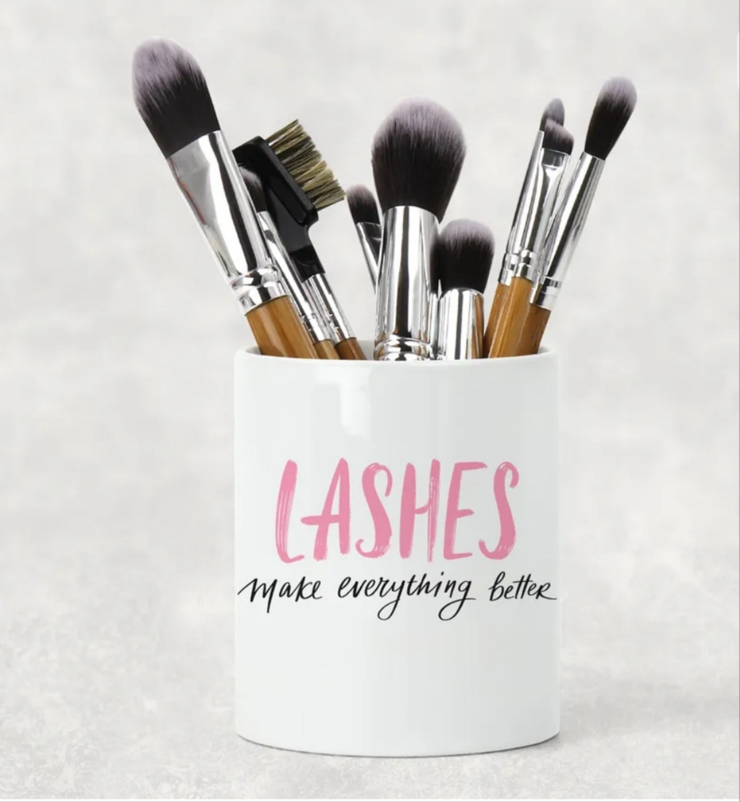 A white ceramic lash brushholder with the words lashes make everything better.