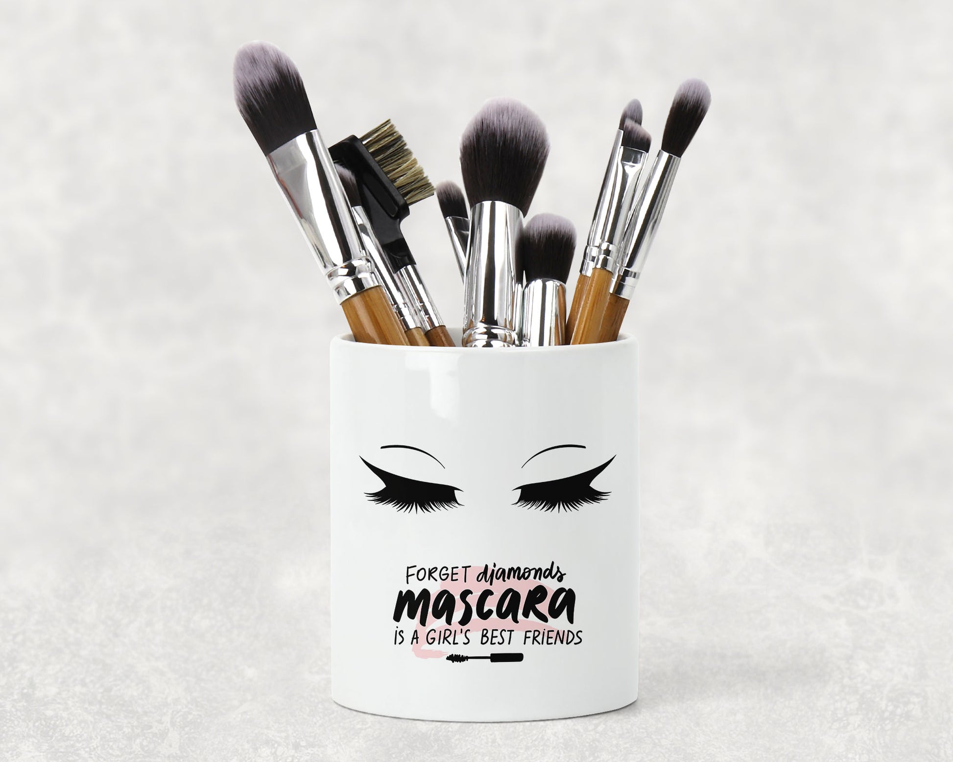 A white ceramic makeup brush holder with the words Forget diamonds mascara is a girls best friend.