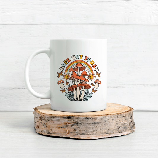 White mug with the words Nope Today with a graphic showing Mushrooms a rainbow, flowers and butterflies . The white mug is displayed on sliced log with a white brick walled background.