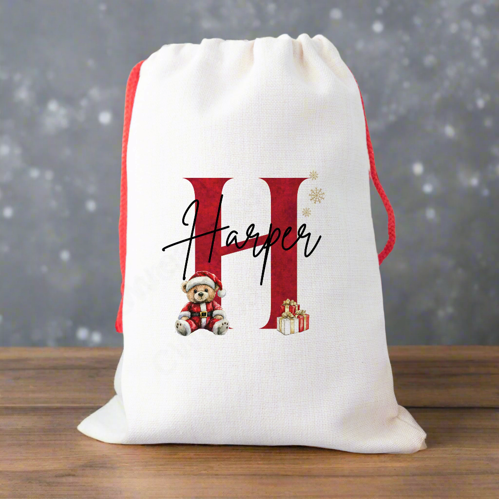 A linen Christmas sack Personalised with a initial and a name with a cute Christmas teddy and presents graphic