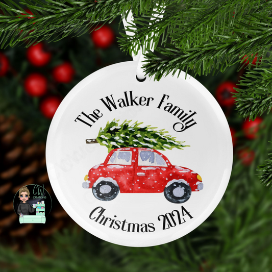 A round Christmas decoration with a graphic of a car with a Christmas tree and snow personalised with a family name and the words Christmas 2024